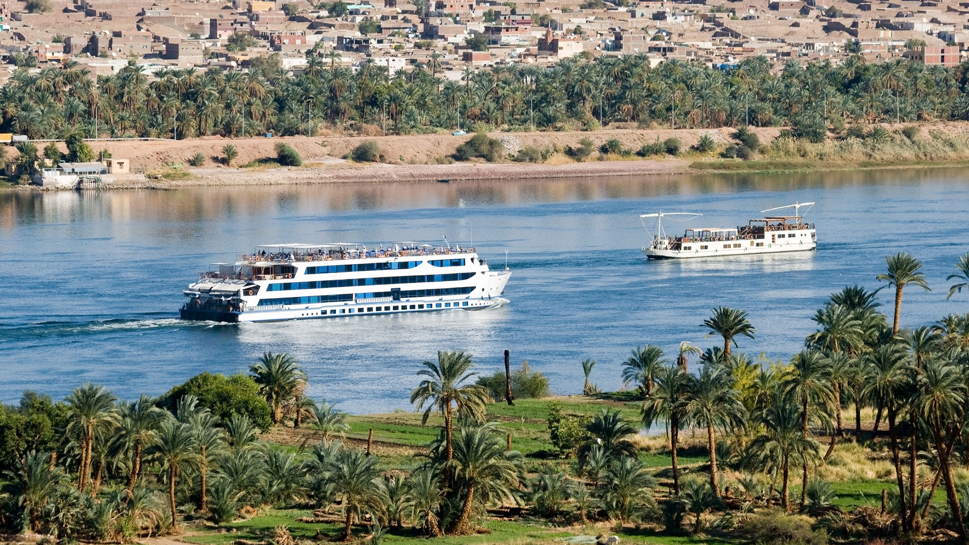 Two cruise ships sailing the Nile past palm groves and a desert town